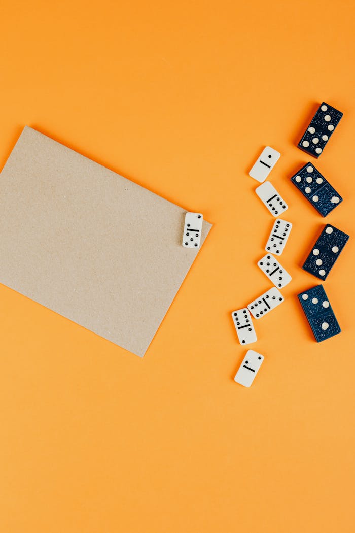 Top view of dominoes scattered on an orange background with empty space for text.